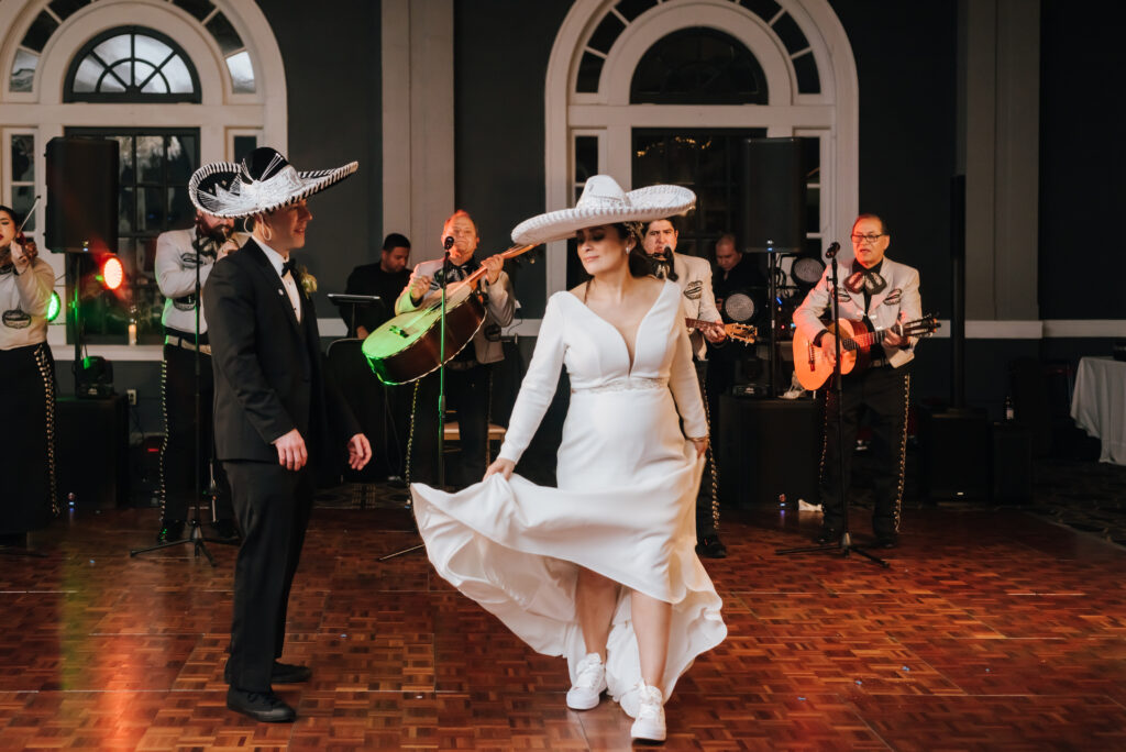A bride and groom wearing mariachi hats dance as the band performs in the background