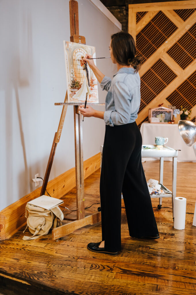 A talented painter carefully adds detail to a painting of the wedding couple during their reception 