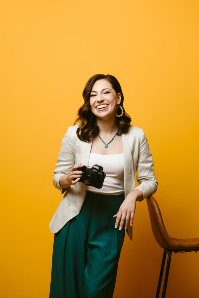 A smiling photographer holds a camera in her hand