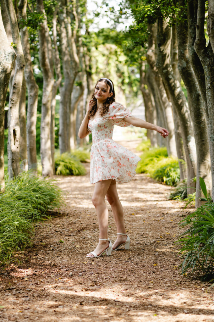 A high school grad tosses her dress behind her as she stands in an open row of trees 