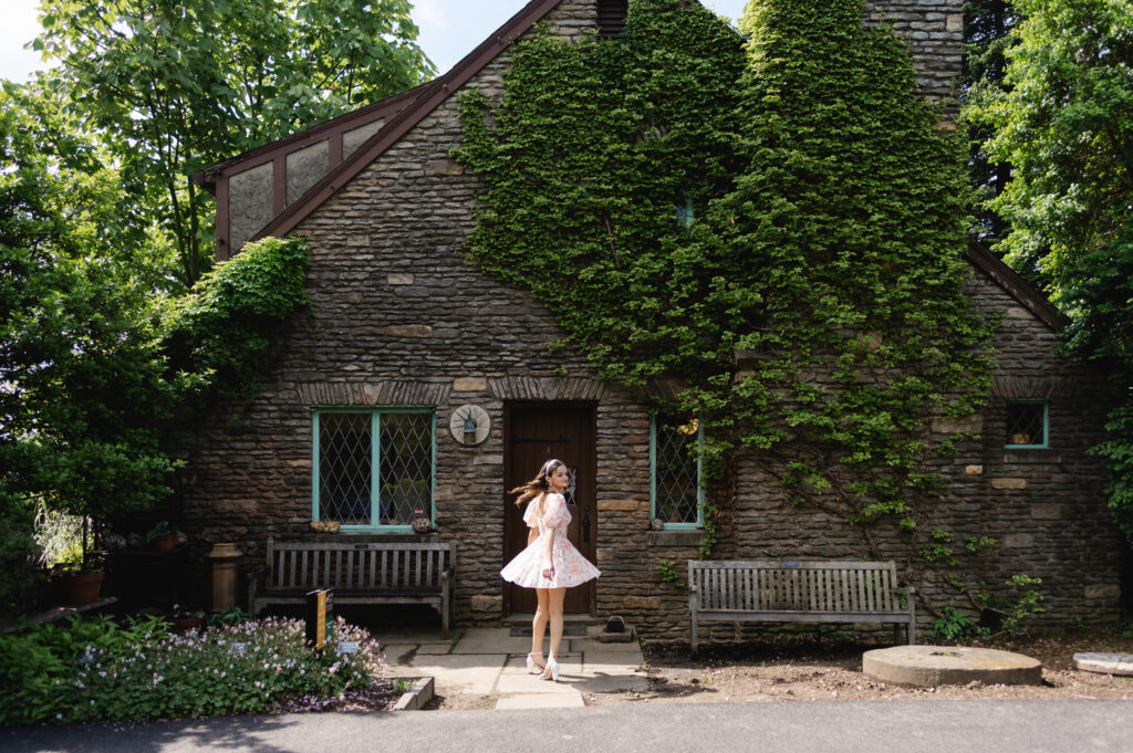 A high school senior twirls in her dress in front of an ivy covered stone cottage