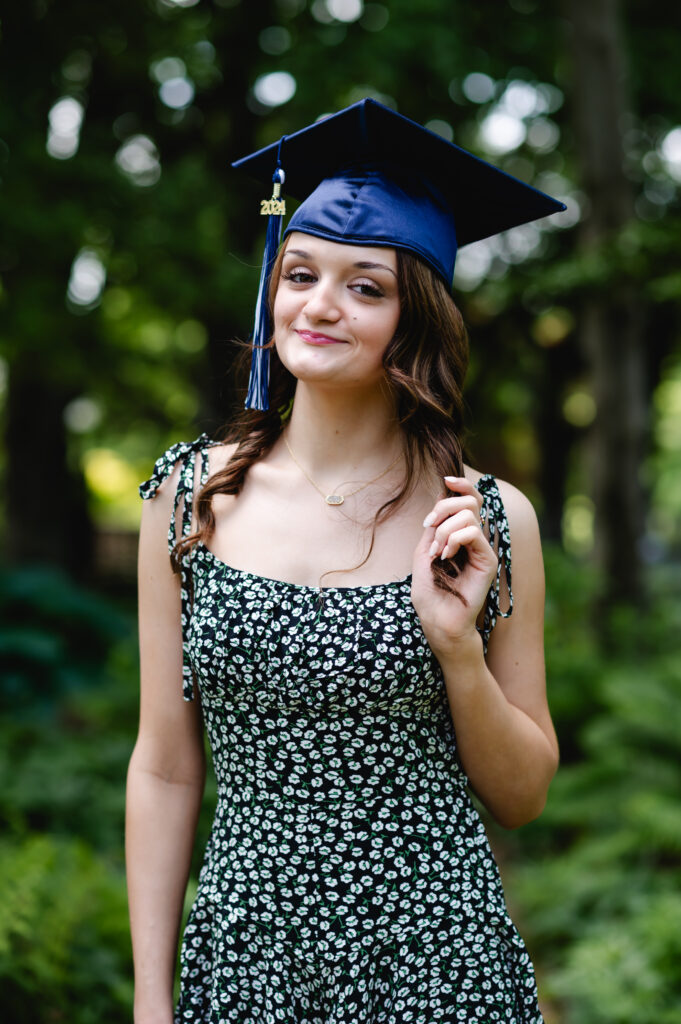 A high school senior poses in Yew Dell Botanical Gardens wearing her graduation cap and a floral print romper