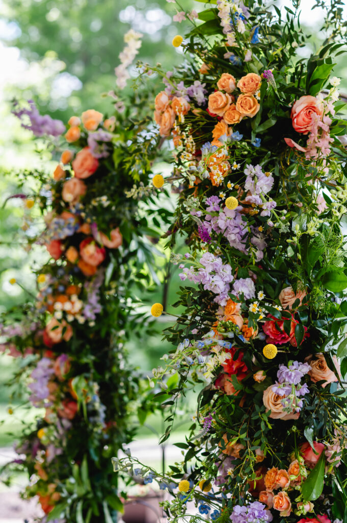 A colorful floral spring arch decorated with orange, pink, purple, yellow and blue flowers 