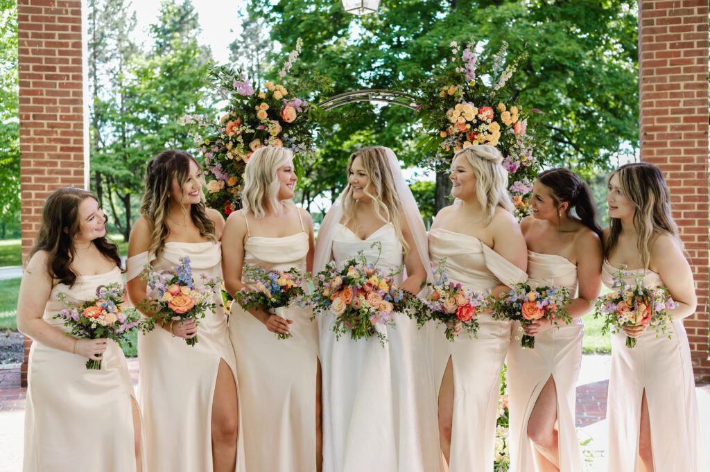 The bridesmaids dressed in satiny pink are smiling at the bride