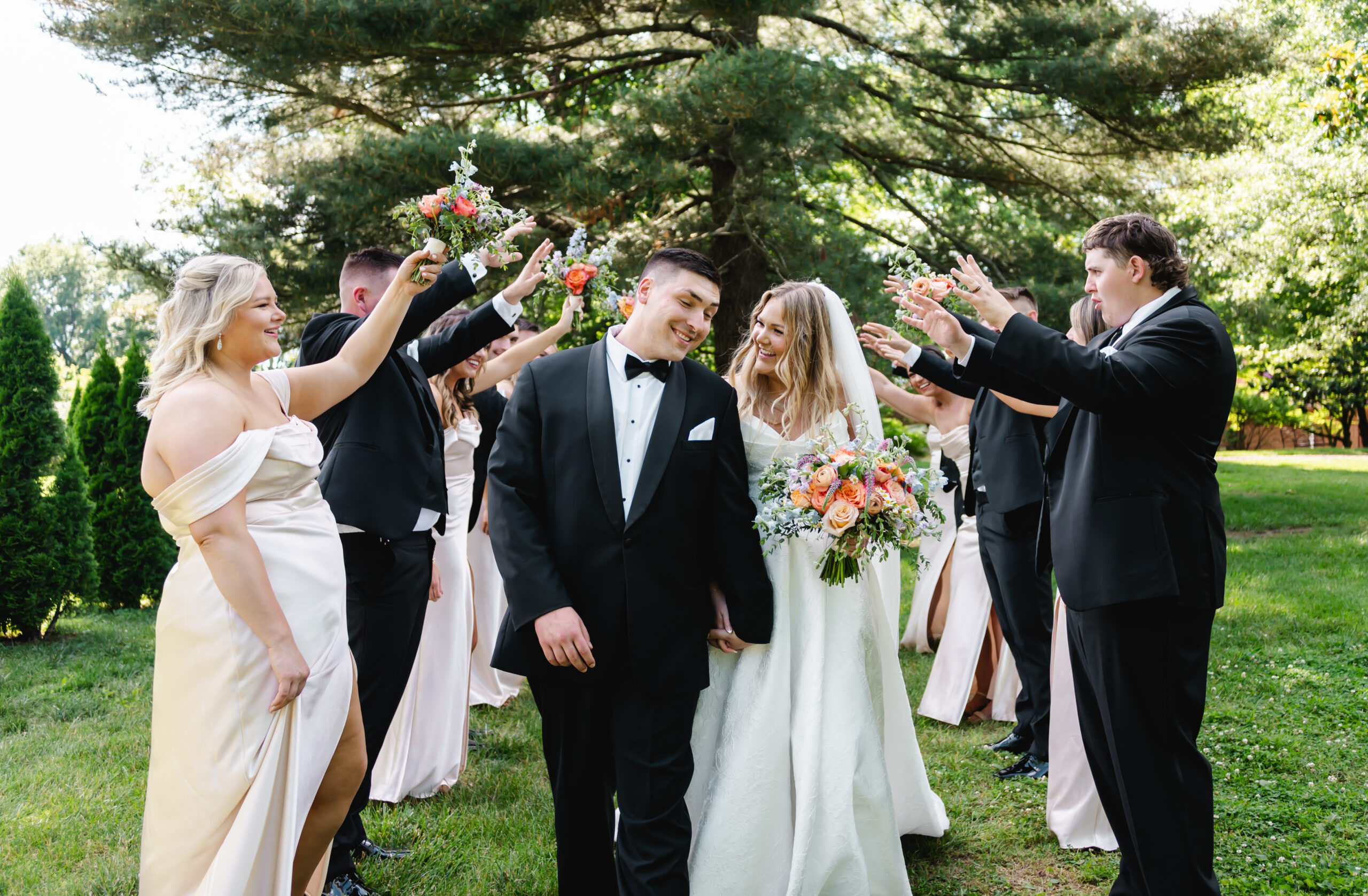 A couple walks hand in hand through a tunnel of their wedding party with their hands and flowers up