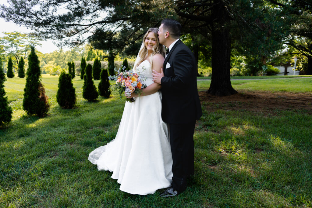 The newlyweds embrace in front of a grove of beautiful landscaped trees