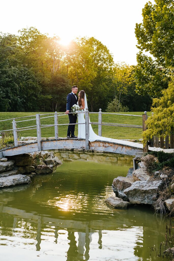 A bride and groom kiss on a bridge over a pond at a Louisville wedding venue.