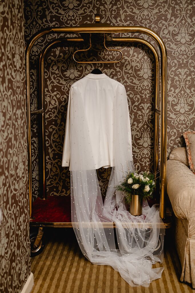 A white wedding jacket hangs from a luggage cart in a Louisville wedding venue.