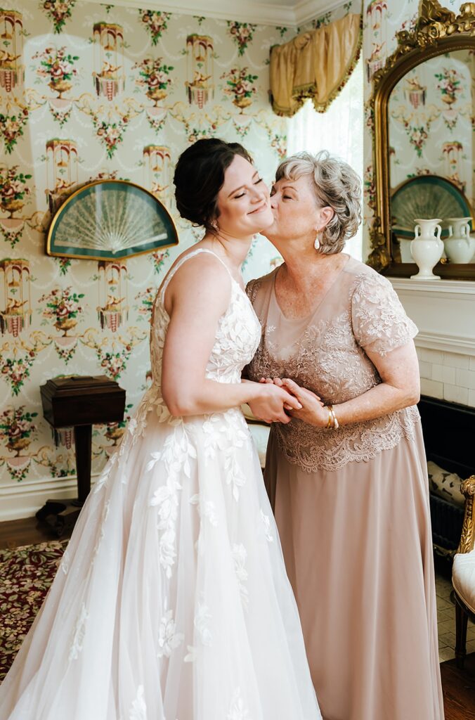 A mother kisses a bride's cheek inside a suite at a Louisville wedding venue.