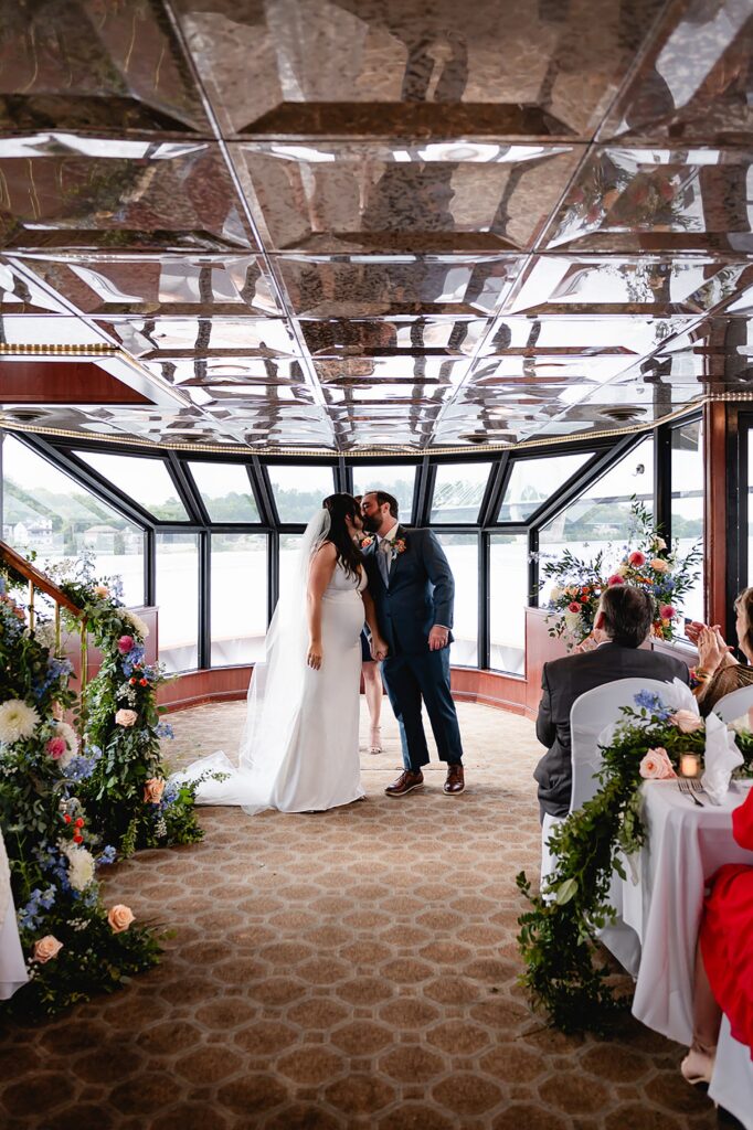 A bride and groom kiss at the end of a wedding ceremony on a private yacht.