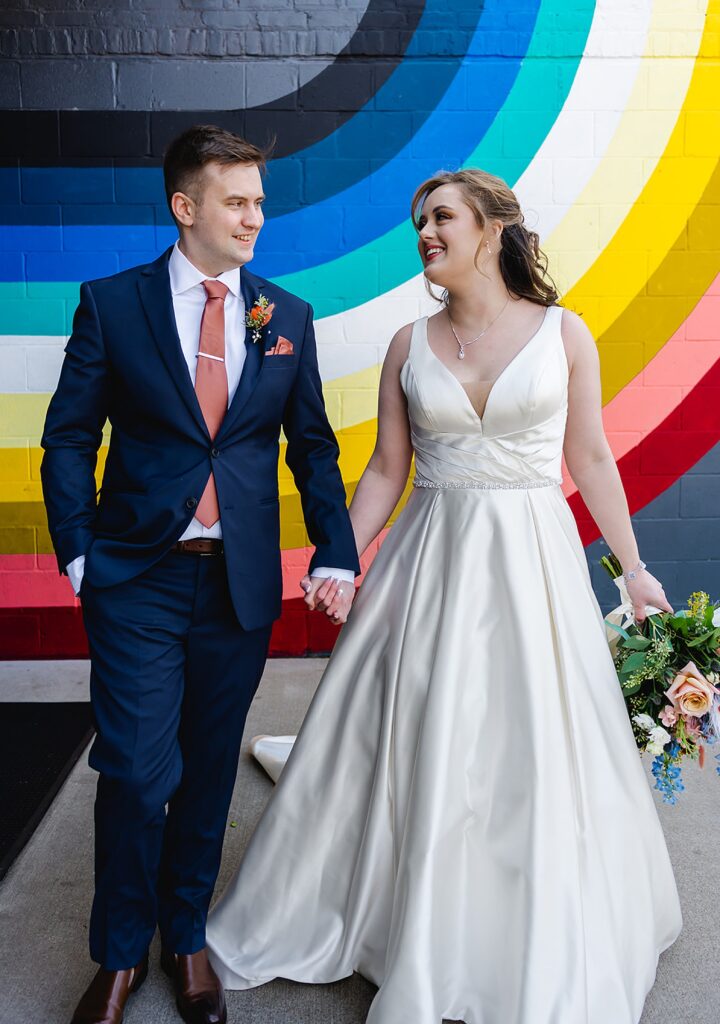 A Kentucky bride and groom pose in front of a rainbow mural.