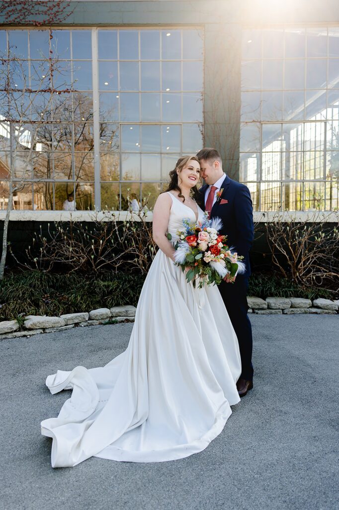 A groom kisses a bride's cheek on a sunny Louisville sidewalk.