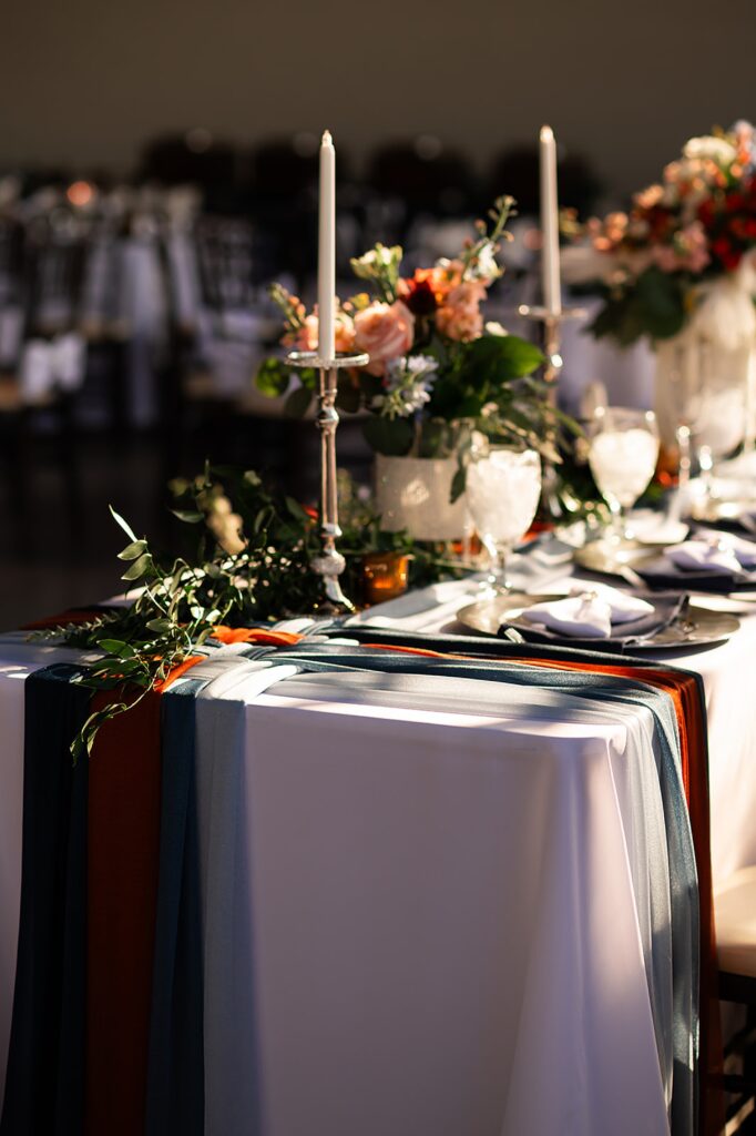 Sun shines on a wedding reception table decorated with ribbons, flowers, and candles.