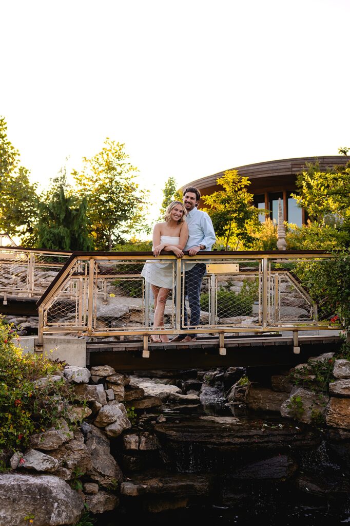 A bride and groom lean on a bridge rail over a creek at a garden wedding in Louisville.