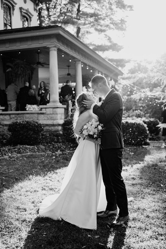 A bride and groom kiss on a lawn outside a Louisville wedding venue.