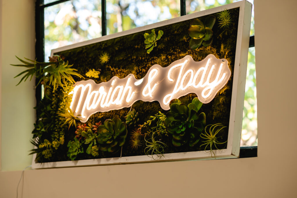 A neon sign that says Mariah and Jody is illuminated, the background behind the names features faux succulents