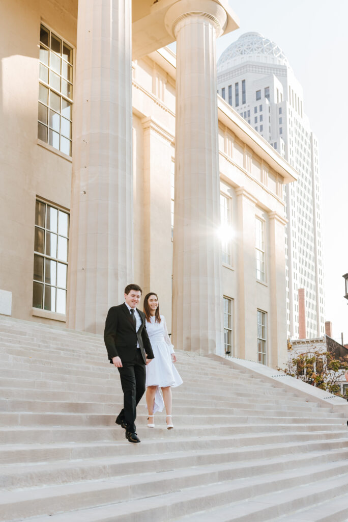 A couple walks hand in hand down the steps of a downtown courthouse building with tall pillars