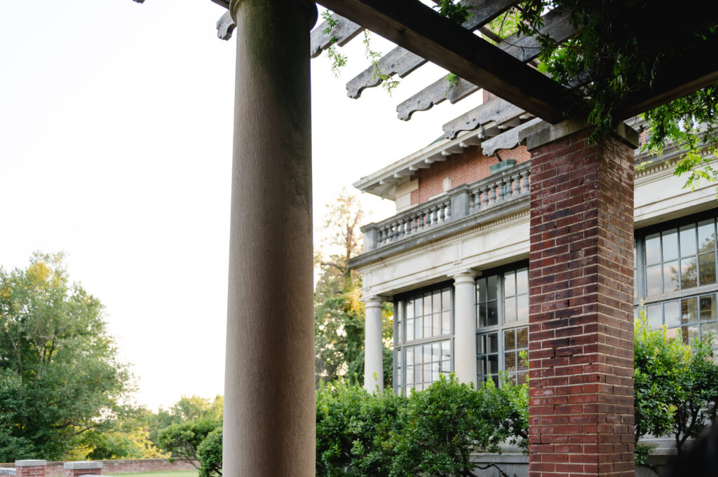 A landscape photo shows the view of the glass sunroom from the ivy colored tresses outside