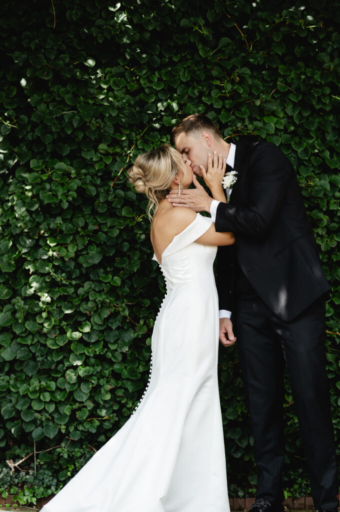 The newlyweds share a kiss in front of the ivy covered brick walls of the garden at Gardencourt