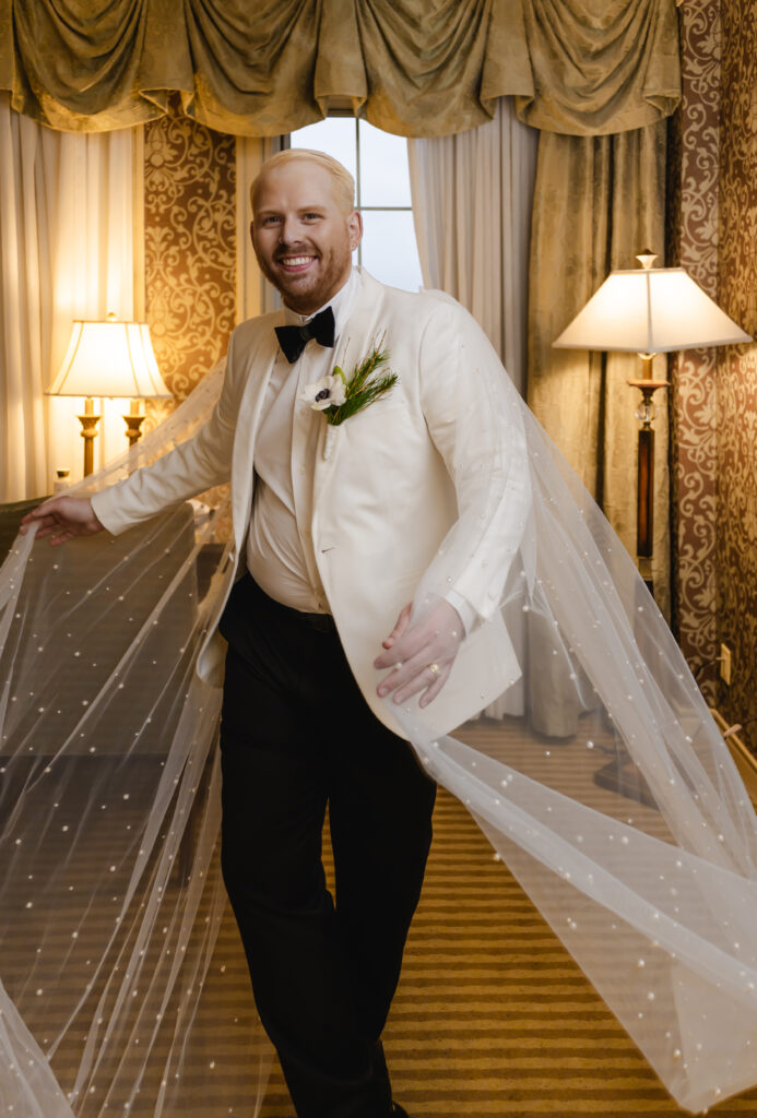 The groom twirls his pearly veil cape and smiles