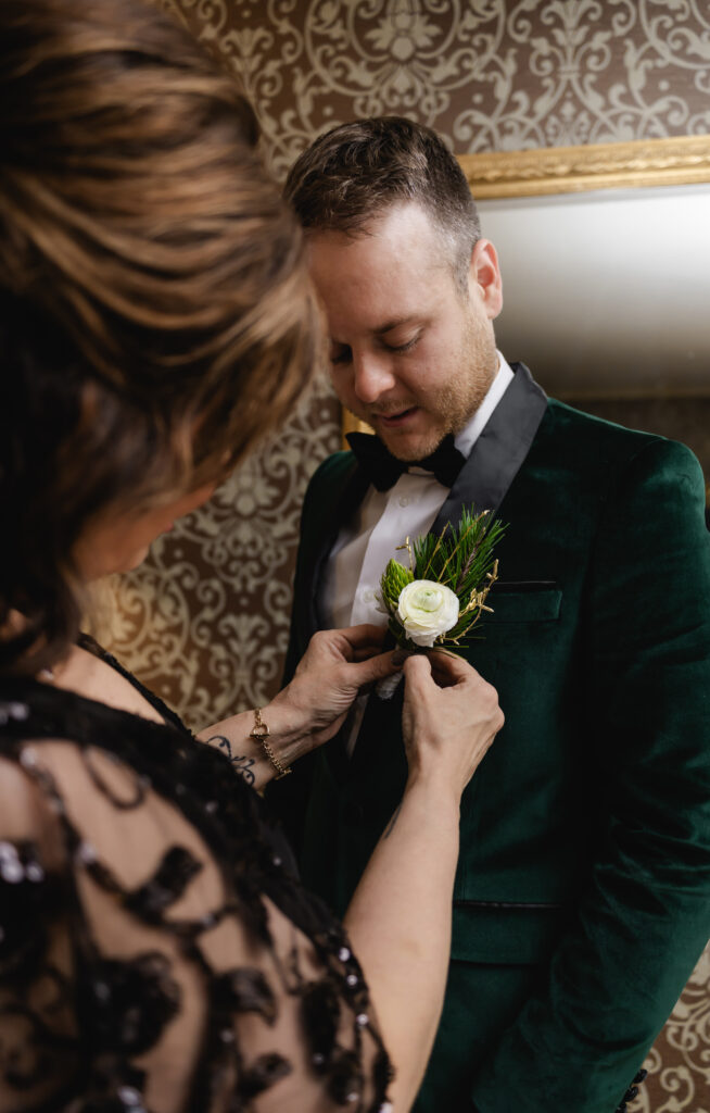 The other groom's mother pins his boutonniere on his emerald tux jacket