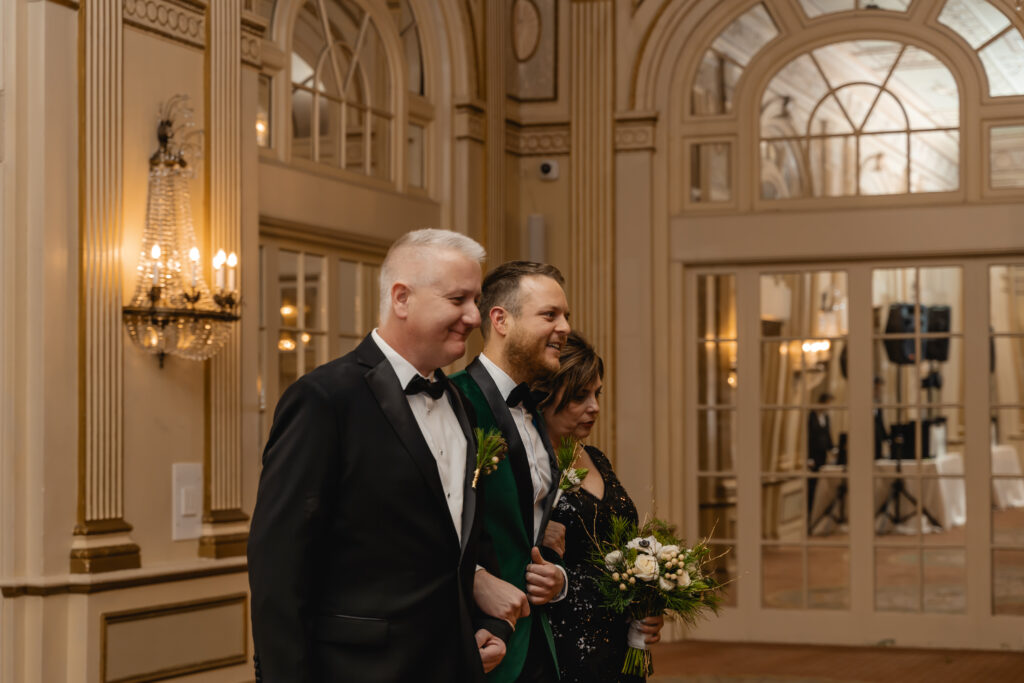 Groom Matthew enters the ballroom of the Brown Hotel with his mother and father on either side