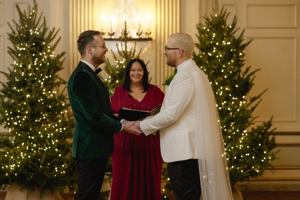 A guest perspective shows the two grooms holding hands and their officiant from the center aisle