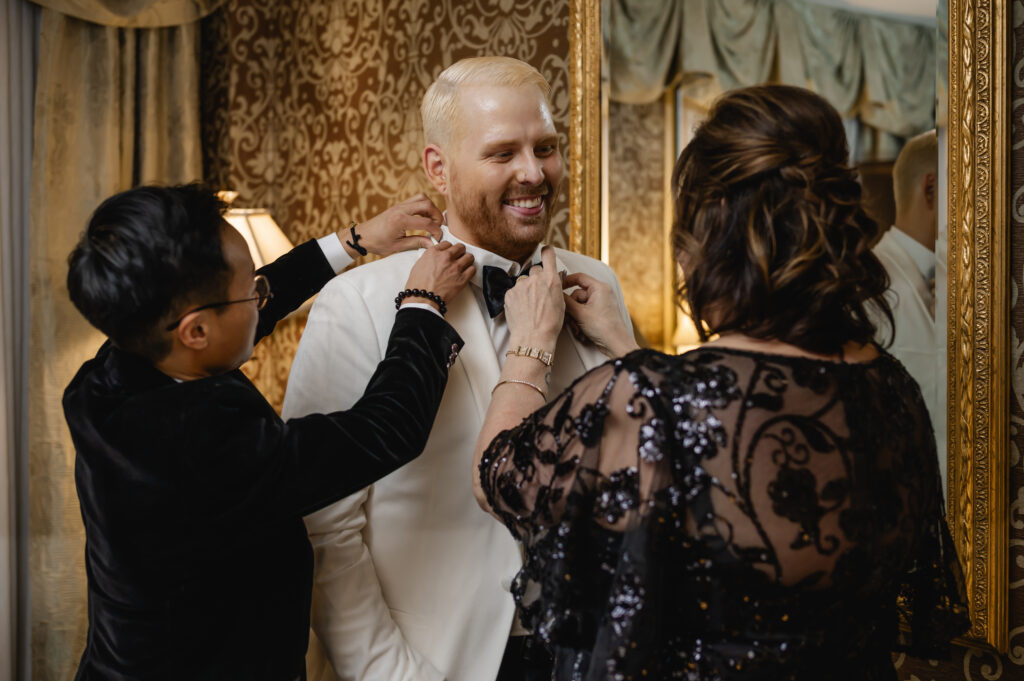 The groom's friend and mother in law help to fix his black bow tie