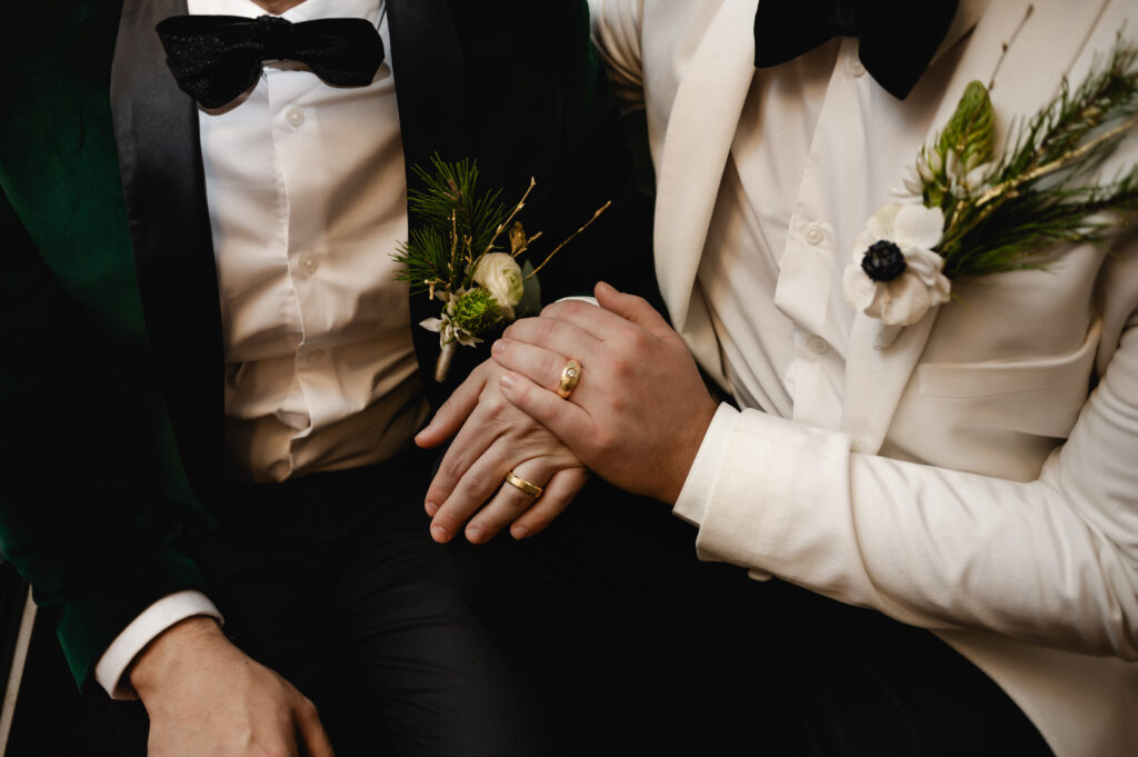 A closeup of the grooms' suits and their ring hands together