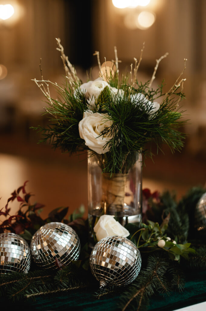 A table centerpiece has a vase with winter florals and small disco balls at the base