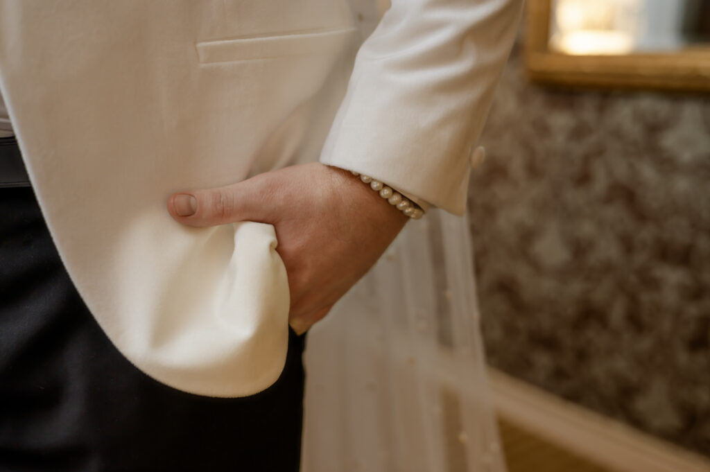 A closeup detail photo of a pearl bracelet, the white tux jacket and pearly veil