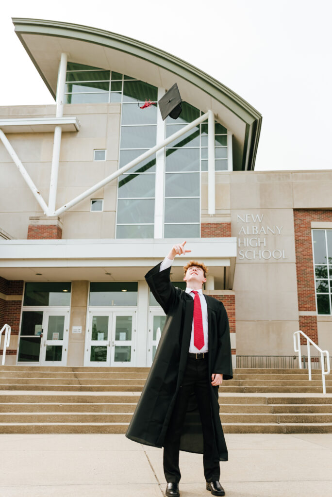 A New Albany High School grad tosses his cap in the air in front of his school