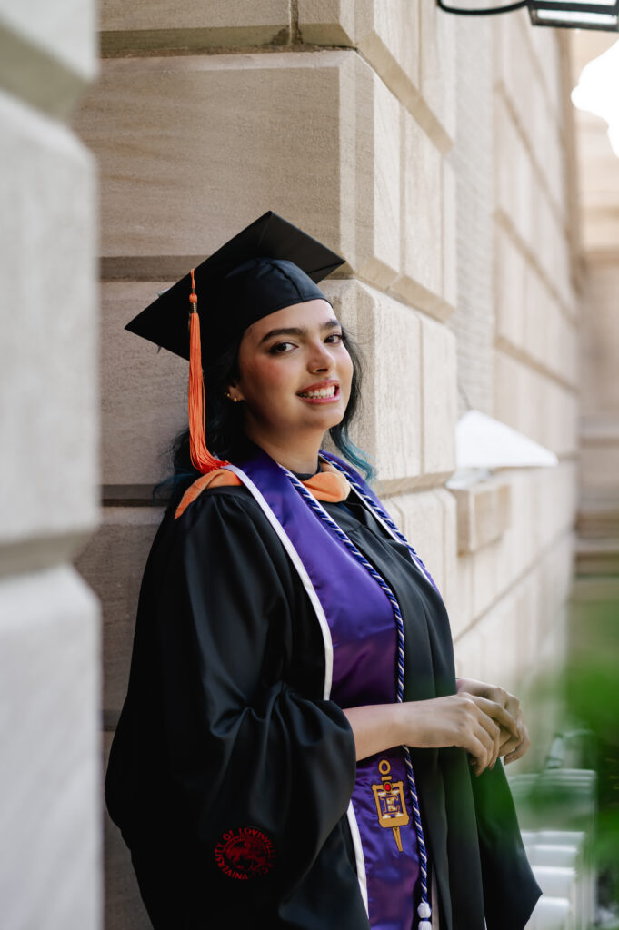 A PhD graduate student proudly flashes a smile as she wears her graduation attire and purple stole. 