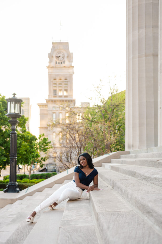 A Black teen girl sits on the steps in front of Louisville Metro Hall at golden hour.
