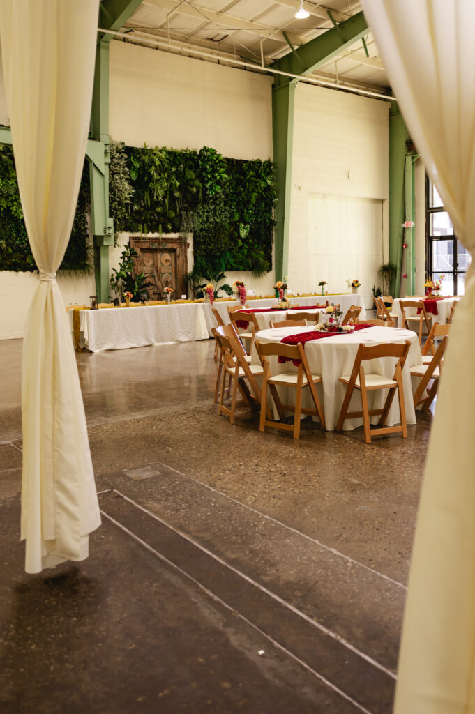 A wide shot of the reception space at Germantown Gables, with the industrial white and green walls, an artificial greenery wall, and white curtains to separate the room.