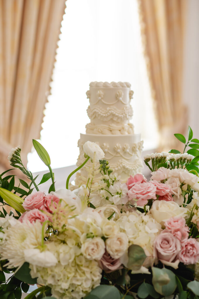 A vintage-inspired three tiered round cake sits among an array of white and pink flowers.