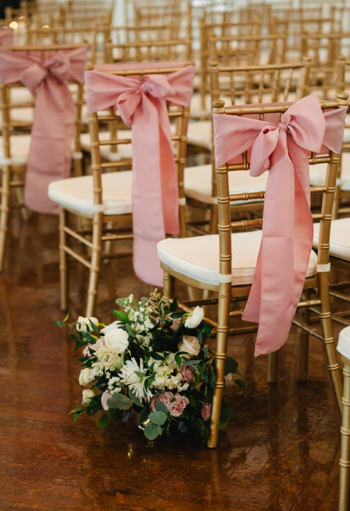 A closeup of gold chiavari chairs with white cushions and pink bows on the back.
