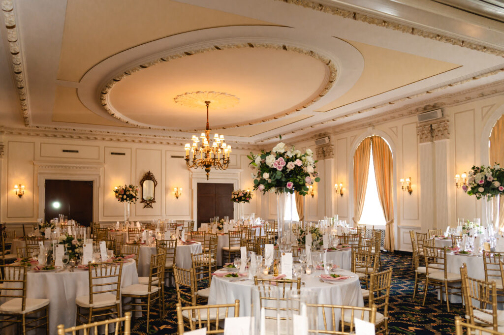 An elevated reception with round tables, tall centerpieces, and ornate ceilings.