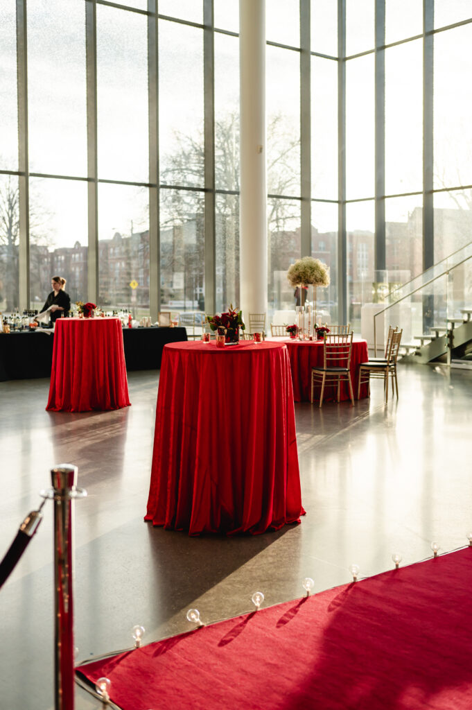 The atrium of the Speed Art Museum is decorated for cocktail hour with high top tables and red tablecloths.
