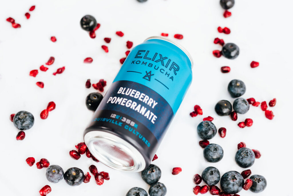 An overhead shot of a can of Blueberry Pomegranate kombucha, surrounded by pomegranate seeds and blueberries on a white background