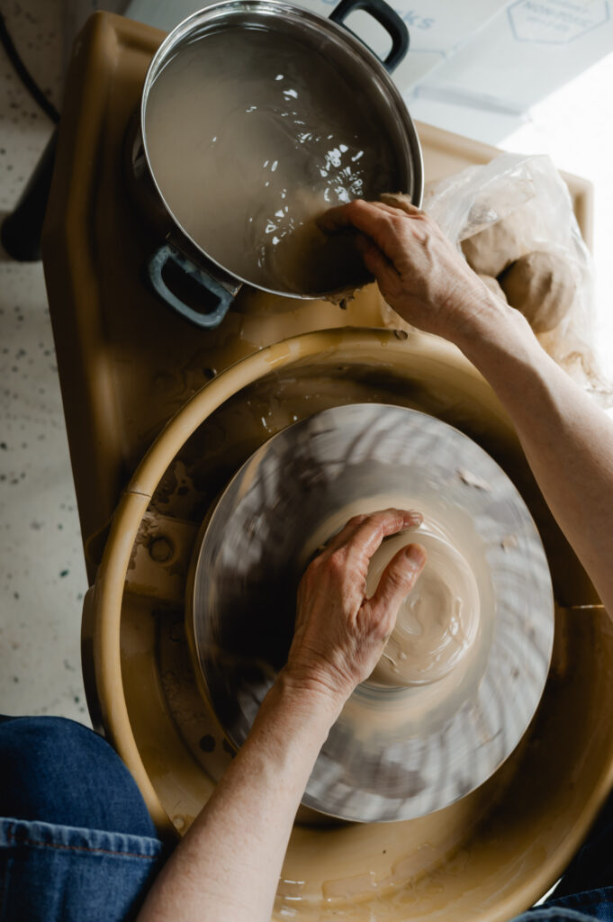 A ceramics artist shapes pottery with one hand, and dips her other hand in a water