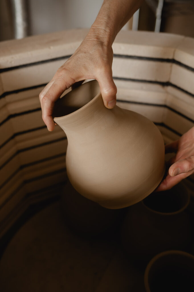 A hand places a piece of pottery inside the kiln