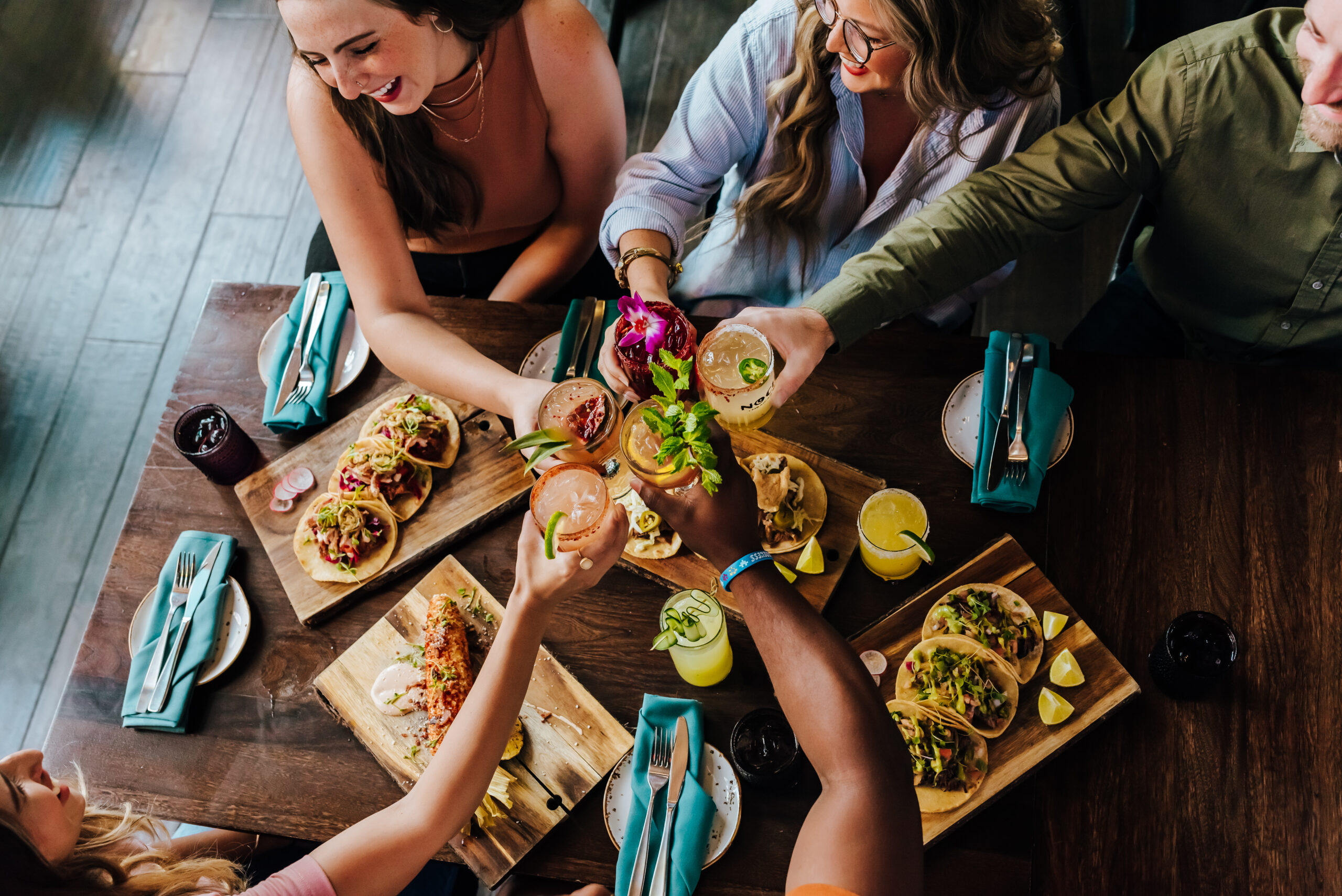 A group of friends do a "cheers" with their drinks as they dine at a Mexican restaurant