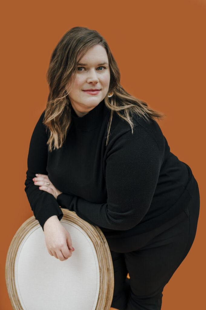 A Louisville professional looks stoically into the camera for her brand photo. She wears all black and rests pensively against a white chair