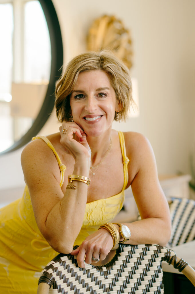 A wardrobe stylist in a butter yellow dress smiles as she poses for a relaxed brand portrait in her home.