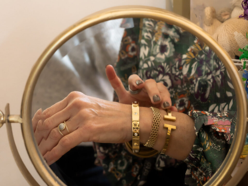 A woman arranges gold bangles on her arm in a mirror reflection at a boutique shop.