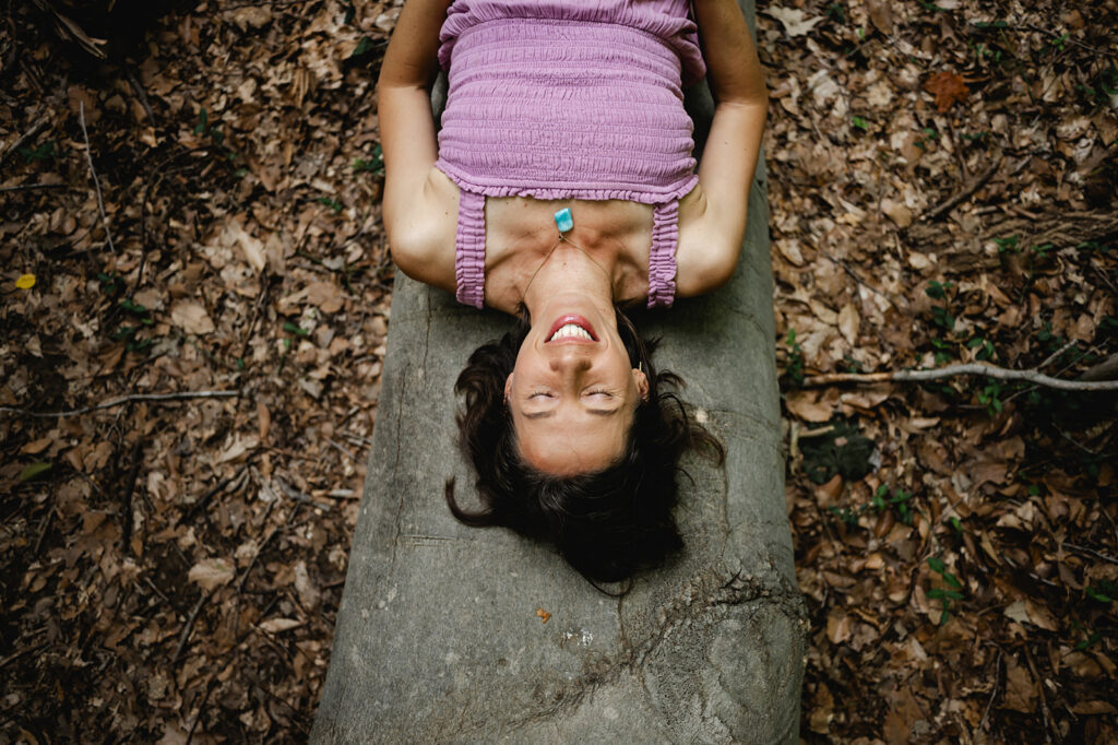 An overhead photo of Ana lying on the log with her face skyward. She closes her eyes and smiles.