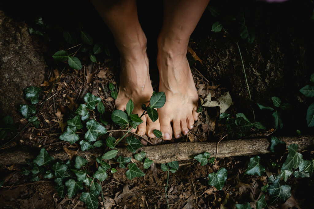 A woman's bare feet are illuminated by the sun on a dark forest path.