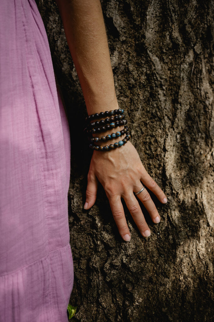A closeup of Ana's tan arm with beaded bracelets from her home, the Dominican Republic, as she rests her arm against the tree behind her.